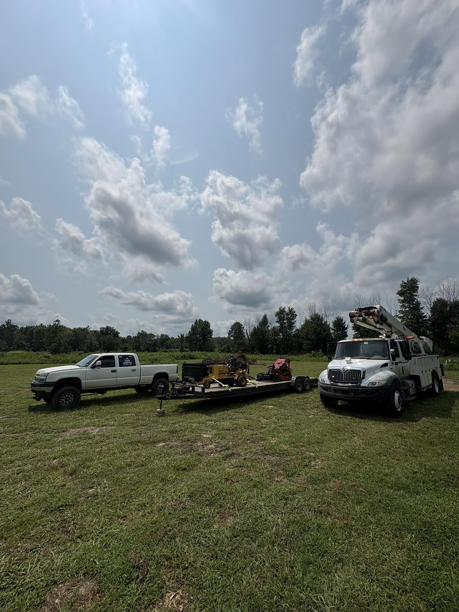 Service pickup, loaded equipment trailer, and bucket truck lined up in a field