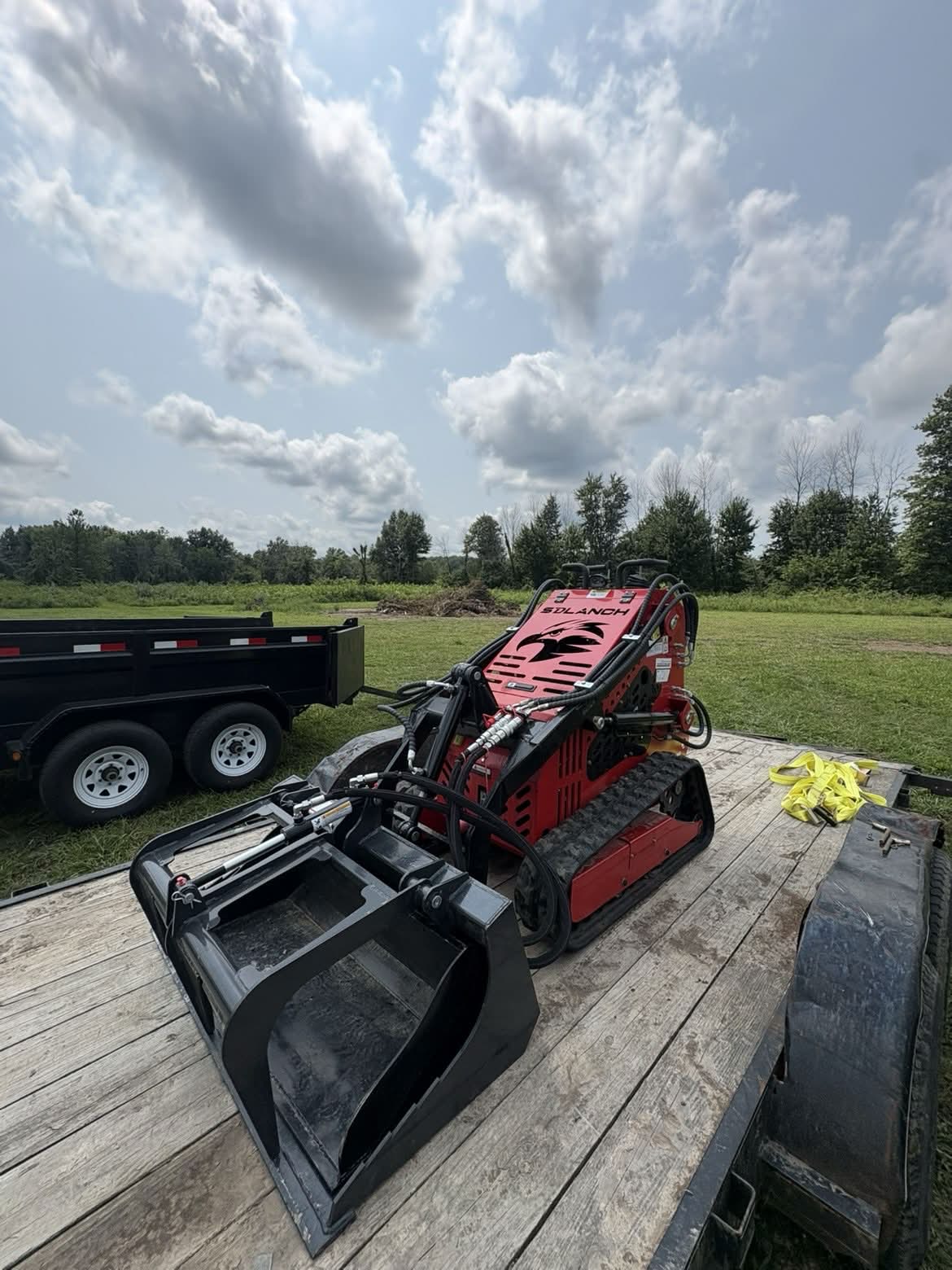 Red mini skid steer with grapple bucket attachment loaded on the trailer