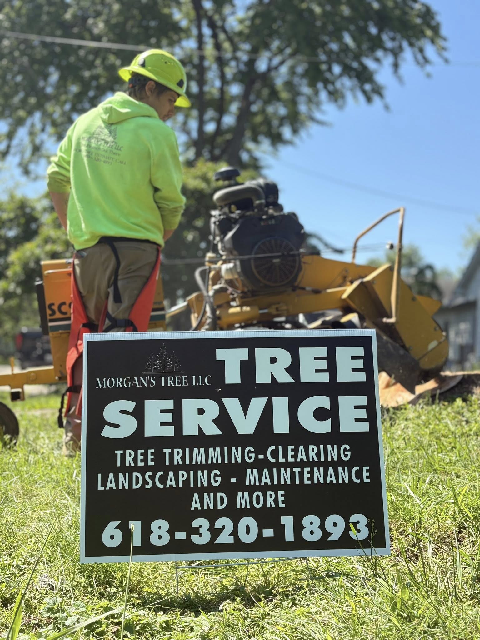 Morgan's Tree LLC crew member running a stump grinder behind the branded yard sign in Olney, IL